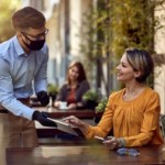 Happy,Woman,Talking,To,A,Waiter,Who,Is,Wearing,Protective